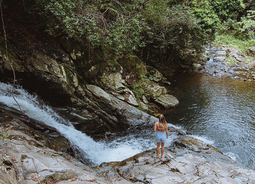 A woman stands next to a waterfall at Currumbin Rock Pools
