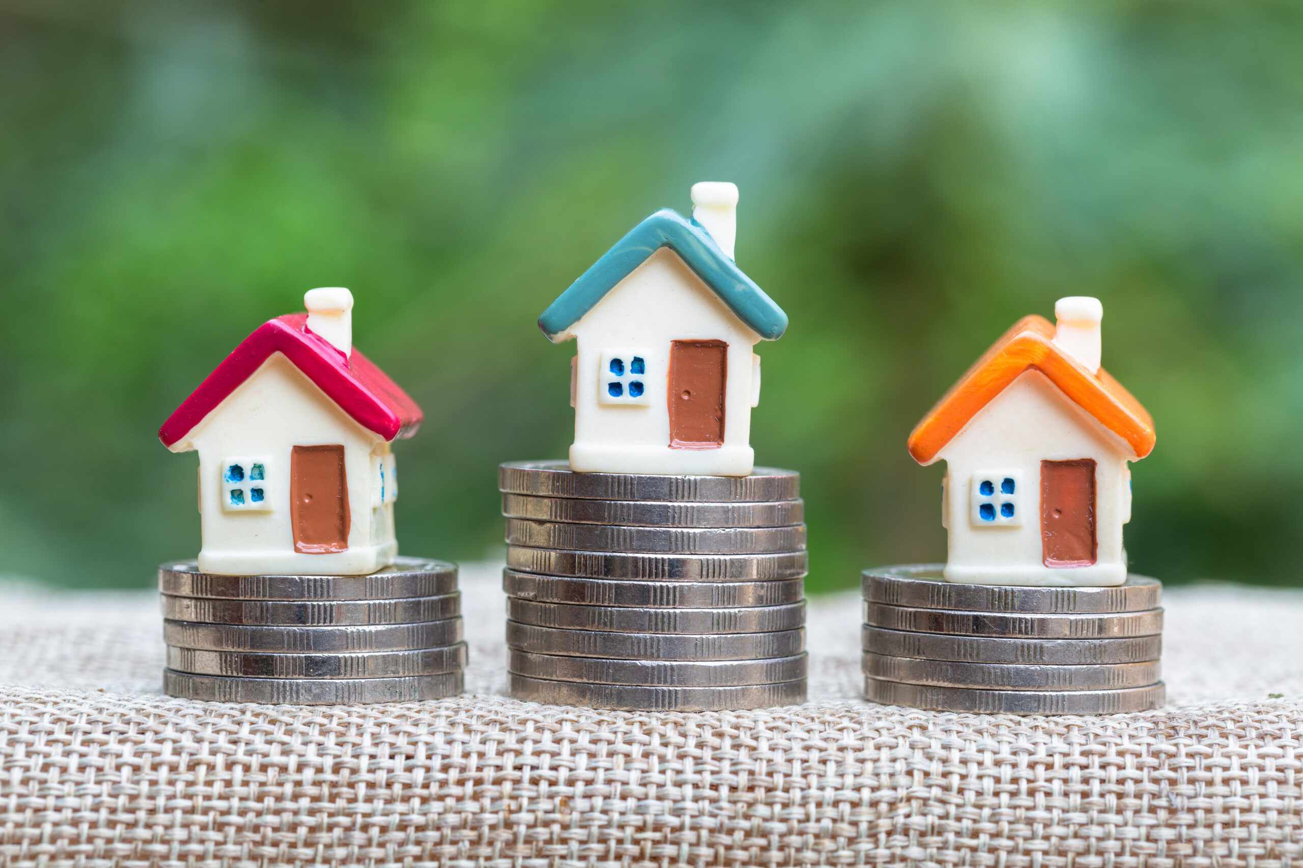 3 small model houses sit on top of piles of coins