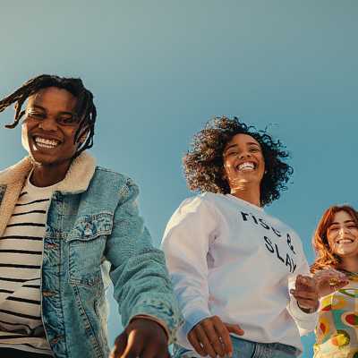 Three young people standing outside, smiling and looking down at the camera