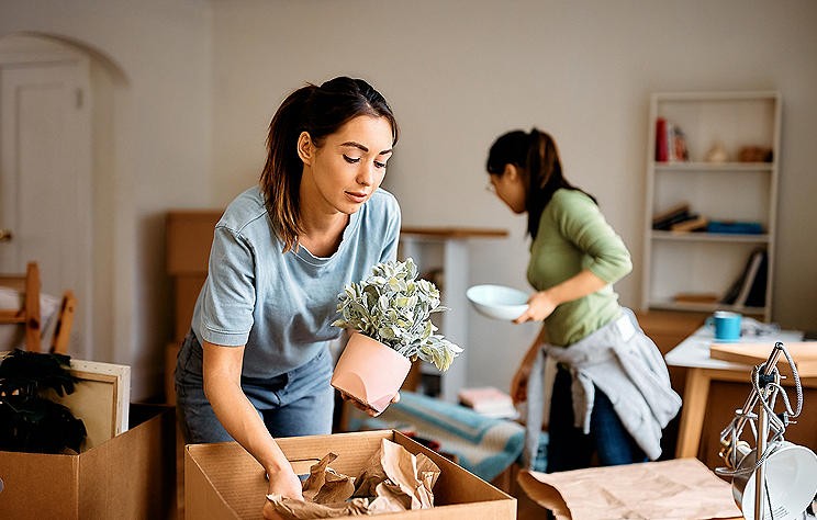 Two women pack household items into moving boxes