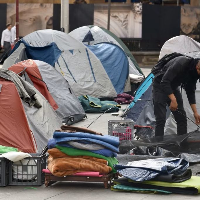 A person is setting up a tent among a group of tents in an urban setting. ABC Radio