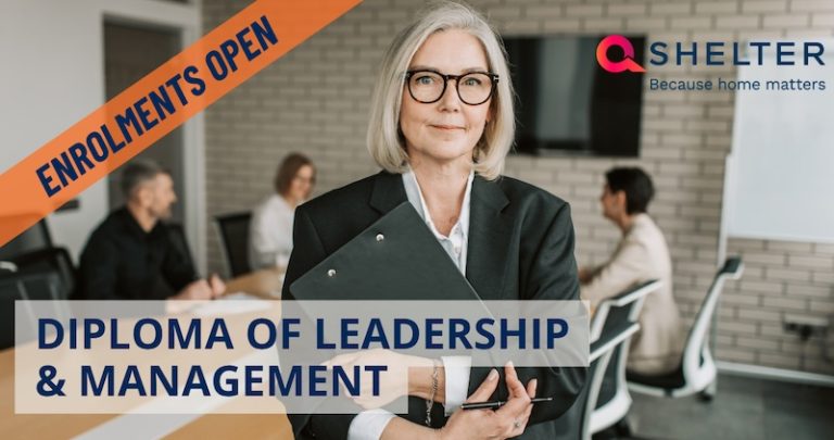 A woman standing in front of a meeting room desk where others are meeting. Promoting Diploma of Leadership and Management for Q Shelter.